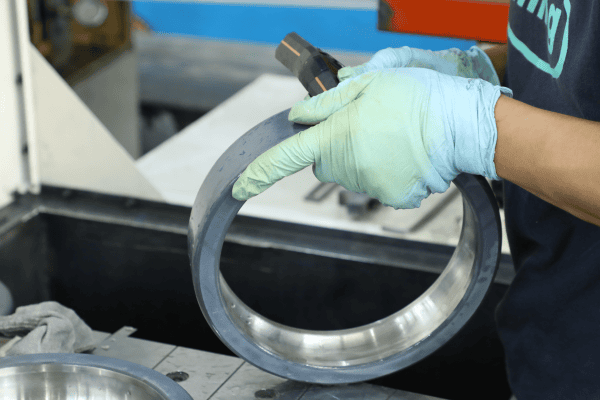 Technician performing manual inspection and calibration on a coated bearing ring in a manufacturing workshop.