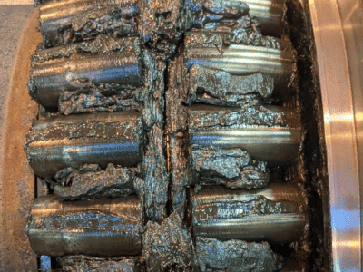 Close-up of a failed double-row wind turbine bearing completely packed with degraded, black, contaminated grease and metallic wear particles.